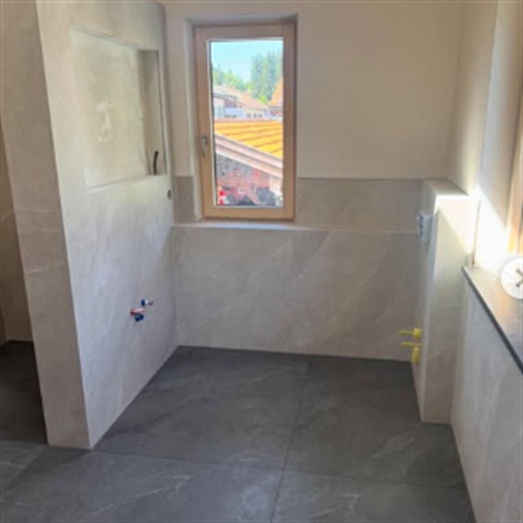 Frisch gefliestes Bad mit hellen Wandplatten und dunklem Bodenformat
