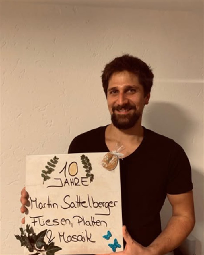 Martin Sattelberger mit einem selbst gestalteten Schild zum zehnjährigen Bestehen seines Betriebs für Fliesen, Platten und Mosaik