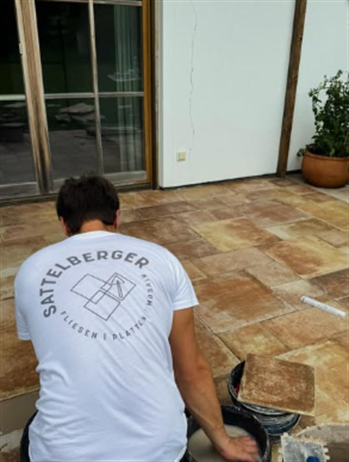 Martin Sattelberger bei der Arbeit auf einer Terrasse, im Rücken das Firmenlogo auf dem Arbeitsshirt